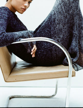 Model sitting with legs tucked in tan leather chair wearing Multi Marl Knit Dress in dark eggplant melange