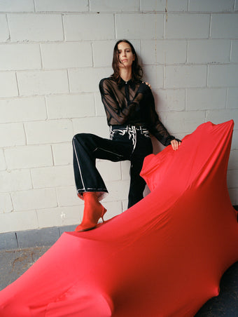 Image of model wearing Ryman Jean in black multi with Smithson Top in Organza Knit in black, standing against motorcycle wrapped in red cover