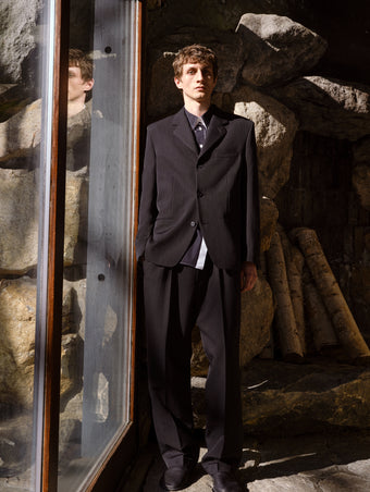 Proenza Schouler Front full length Editorial image of model wearing James Jacket in Wool Suiting in Black against Rock wall background.