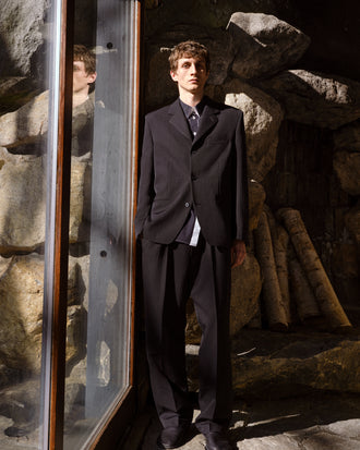 Proenza Schouler Front full length Editorial image of model wearing James Jacket in Wool Suiting in Black against Rock wall background.
