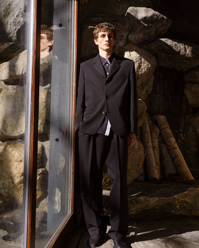 Proenza Schouler Front full length Editorial image of model wearing James Jacket in Wool Suiting in Black against Rock wall background.