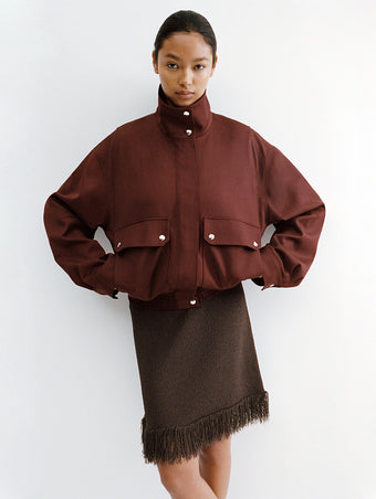 Proenza Schouler Editorial image of model standing against white wall wearing the Aviva Jacket in Wool Gabardine in Oxblood with the Saski Dress in Cotton in Textured Fringe in Earth