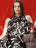 Proenza Schouler campaign image of model sitting in front of red background wearing Sybella Dress in Metalasse Silk Linen in Black Multi with the Bucket Bag in Raffia in plum