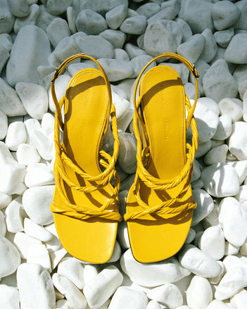 Still life image of bright yellow twist sandals against white rocks
