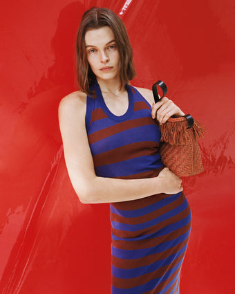 Model wearing Frann dress leaning against red lacquered dress holding Raffia bag
