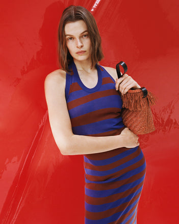 Model wearing Frann dress leaning against red lacquered dress holding Raffia bag