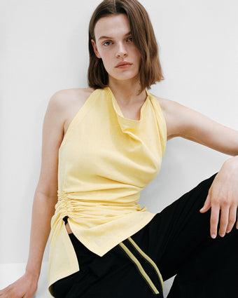 Image of model sitting in Melia top and Lissia pants against a white wall and white floor