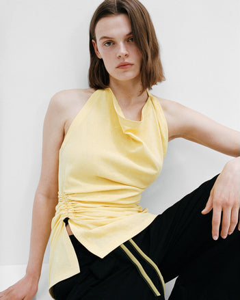 Image of model sitting in Melia top and Lissia pants against a white wall and white floor