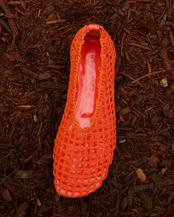 Orange crochet slant flat still life image on a backdrop of dirt and mulch