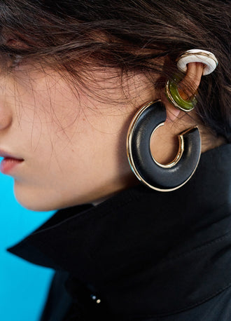 Proenza Schouler Editorial image of model wearing Leather Hoop Earrings in black and Mini Hoop Earrings in olive and optic white