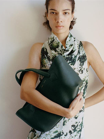 Proenza Schouler Front full length image of model wearing Adelide Dress in Printed Silk Viscose in Dark Green Multi holding the East West Chelsea Tote in Pebbled Calf Bottle.