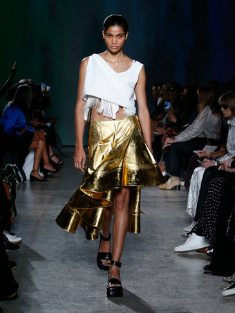model wearing white top and gold skirt