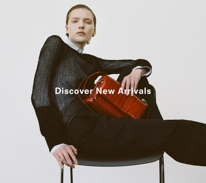 Cropped image of a model wearing Allen Shirt in Crinkled Cotton Gabardine in sky blue, Willa Sweater in Sheer Mesh in black, carrying a City Bg in Eel in rosewood, 'Discover New Arrivals' overlaid