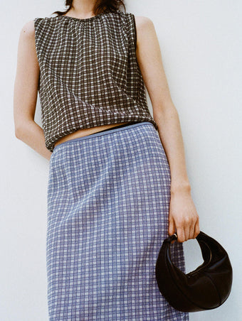 Cropped image of a model leaning against a white backdrop, wearing Bradley Crewneck in Plaid Knit in Off White/Black and Lori Knit Skirt in Plaid Knit Off White/Denim