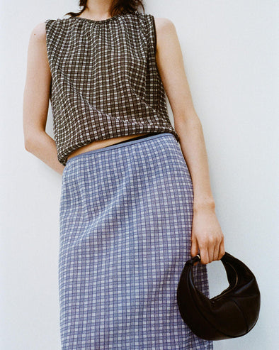 Cropped image of a model leaning against a white backdrop, wearing Bradley Crewneck in Plaid Knit in Off White/Black and Lori Knit Skirt in Plaid Knit Off White/Denim