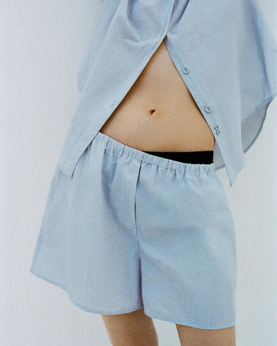 Cropped image of a model leaning against a white backdrop, wearing Caroline Shirt in Linen Shirting and Jana Short in Linen Shirting in Light Oxford Melange