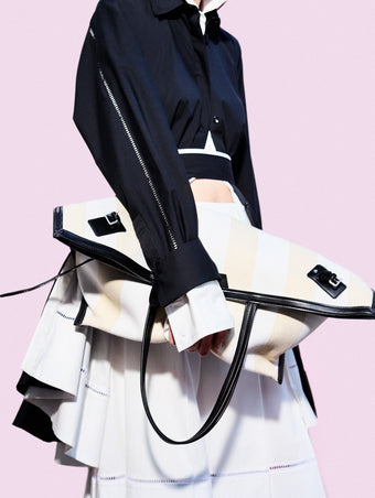 Cropped image of model standing against pink backdrop, wearing Laci Skirt in Eco Cotton Poplin in White holding Days Carryall in Striped Canvas in Resin/White