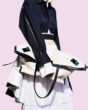 Cropped image of model standing against pink backdrop, wearing Laci Skirt in Eco Cotton Poplin in White holding Days Carryall in Striped Canvas in Resin/White