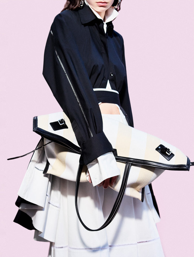 Cropped image of model standing against pink backdrop, wearing Laci Skirt in Eco Cotton Poplin in White holding Days Carryall in Striped Canvas in Resin/White