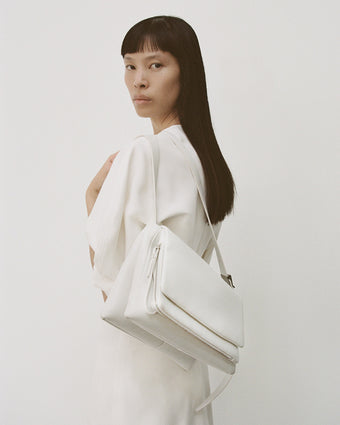 Cropped image of model wearing Goldie Dress in Matte Viscose Crepe in white, carrying the City Messenger Bag in optic white