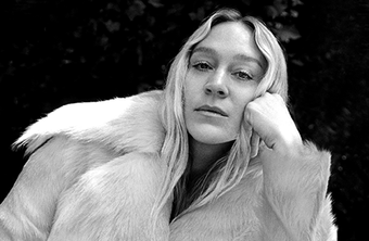 black and white image of Chloe Sevigny sitting outdoors leaning on a picnic table with gingham table cloth 