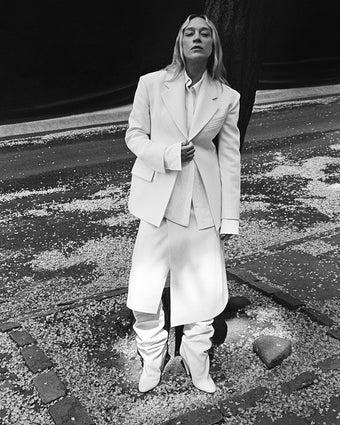 Chloe Sevigny leaning against flowering tree in Wool Twill Jacket and Skirt in bone