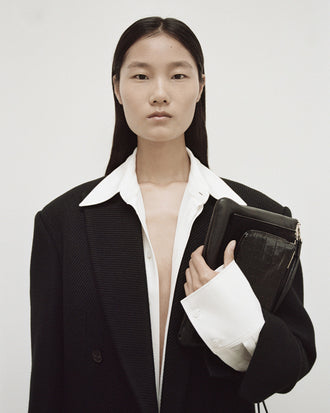 Cropped image of model in Henri Coat in black, carrying Triple Zip Pouch in black