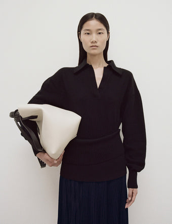 Model in Jeanne Sweater In Eco Cashmere in black and Sheer Pleated Jersey Skirt with Knit Yoke in navy, carrying Large Chelsea Tote in ivory/black