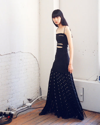 4x5 image of model Shuqi Lan wearing a dress behind-the-scenes of the SS25 runway show with carwash panels and silver eyelets against a white brick wall