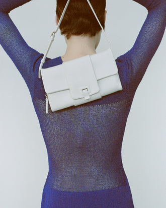 Cropped image of model wearing Anita Dress in Knit Sheer Mesh in bright blue, carrying Flip Shoulder Bag in white.