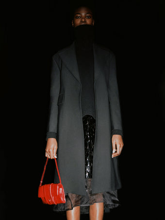 Cropped image of model wearing Irene Dress in Resin Embroidered Organza in black with Sandra Turtleneck in Eco Doubleface Cashmere in black, carrying a Flip Shoulder Bag in Eel in rosewood.