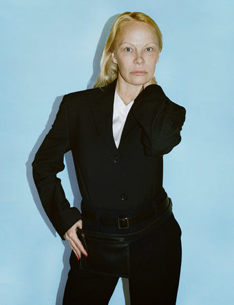 Cropped image of Pamela Anderson in Devon Jacket and Otis Pant in black Viscose Wool, with black Belt Bag layered over