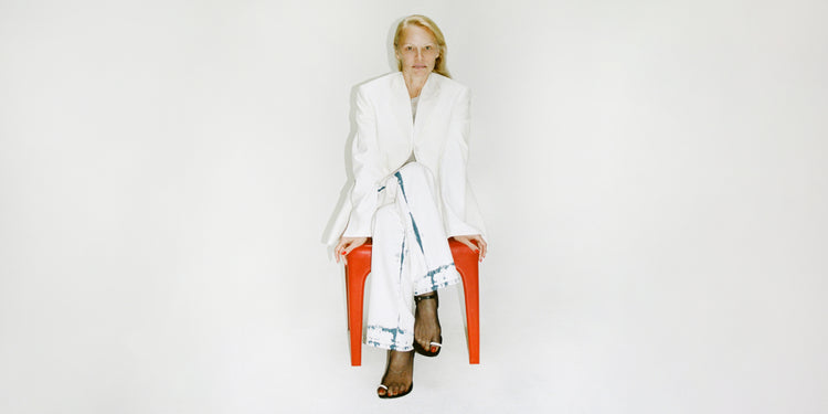 Pamela Anderson sitting in a red chair wearing Proenza Schouler Spring 2024 Collection's white Sandis Jacket in Cotton Viscose and bleach-out Ellsworth Jean 