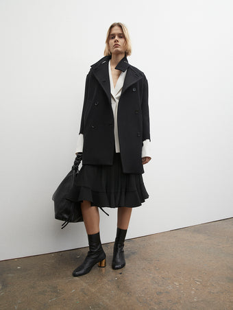 PF23 Collection Look 26: Black Technical Gabardine Peacoat, White Viscose Suiting Jacket, Black Crepe Jersey Skirt, Black Drawstring Shoulder Bag, and Black Sculpt Ankle Boots with Gold Heel