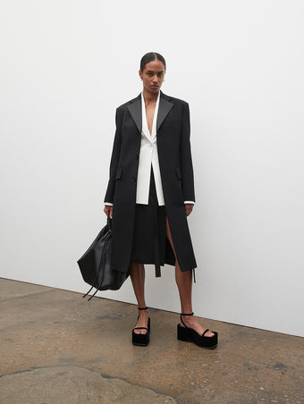 PF23 Collection Look 03: Black Satin Lapel Wool Coat, White Viscose Suiting Jacket, Black Crepe Chiffon Skirt, Black Drawstring Shoulder Bag, and Black Velvet Square Platform Sandals