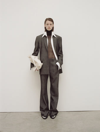 PS24 Look 01 - Black Sheer Viscose Knit Top, Off White Maya Shirt in Textured Marocaine, Grey Melange Barbara Pant in Melange Wool, Grey Melange Laurie Jacket, and Ivory Medium Drawstring Shoulder Bag.
