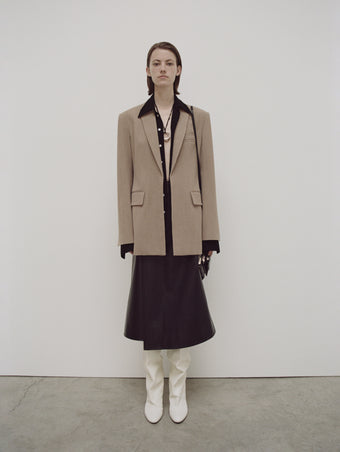 PS24 Look 19 - Black Maya Shirt in Textured Marocaine, Black Helen Wrap Skirt in Leather, Khaki Melange Laurie Jacket, Black Triple Zip Pouch, Cream Cone Boots, and Gold/gold/silver 3-ring Pendant