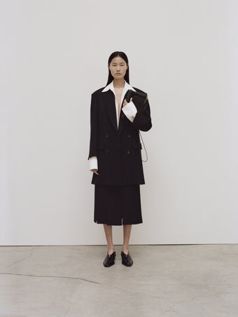 PS24 Look 04 - Off White Maya Shirt in Textured Marocaine, Black Diane Skirt, Black Henri Coat, Black Triple Zip Pouch, and Black Bronco Mules.