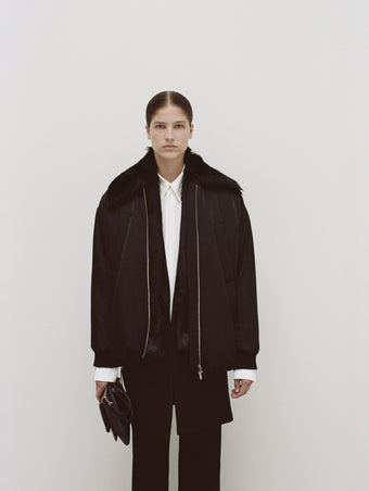PS24 Look 05 - Off White Maya Shirt in Textured Marocaine, Black Barbara Pant in Textured Wool Twill, Black Ray Bomber in Recycled Nylon Twill, Black Henri Coat, Deep Navy/garnet/mocha Triple Zip Pouch, and Black Bronco Ankle Boots.