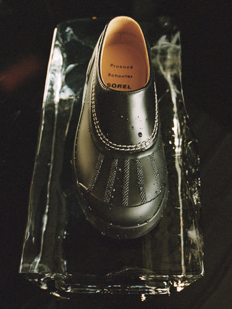 Aerial image of SchoulerSOREL x Proenza Schouler Caribou Mules in black/chalk, sitting on block of ice