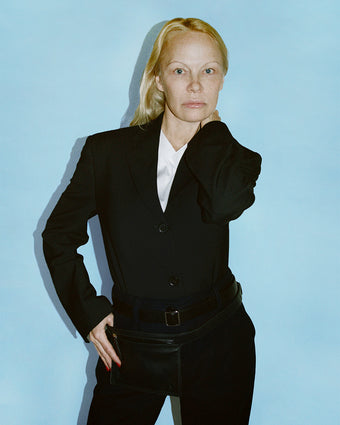Cropped image of Pamela Anderson in Devon Jacket and Otis Pant in black Viscose Wool, with black Belt Bag layered over