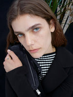 Cropped image of model wearing Prescott Top in Matte Viscose Crepe in black and Marine Jacket in Bi-Stretch Suiting in black, holding Silo Bag in Kid Suede in navy