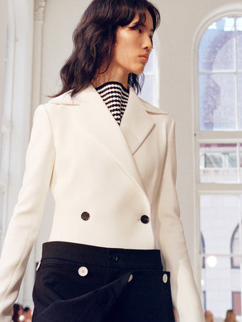 Model walking Proenza Schouler SS25 Runway show wearing Marine Jacket in Bi-Stretch Suiting in off white and Oliver Pant in Wool Gabardine in black