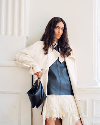 Model wearing Sabina Coat in Lacquered Leather in ecru and Noa Top in Textured Leather in black, carrying Tetra Bag in black
