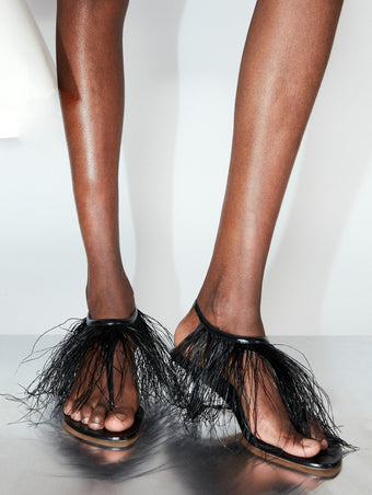 Cropped image of model wearing Tee Thong Feather Sandals in black