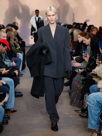 Model in Grey Melange Wool Jacket, Grey Melange Wool Trouser, Charcoal Melange Wool Boucle Coat, Black Bronco Ankle Boots, and Black Leather Gloves