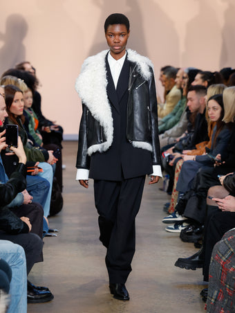 Model in Black Leather Shearling Motorcycle Jacket, Black Wool Stretch Suiting Jacket, White Crushed Matte Satin Shirt, Black Wool Stretch Suiting Trouser, and Black Bronco Ankle Boots