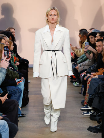 Model in Bone Wool Twill Jacket, White Crushed Matte Satin Shirt, Bone Wool Twill Skirt, Cream Cone Over The Knee Boots, and Black Smooth Nappa Strobel Belt
