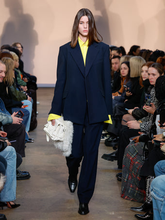 Model in Navy Melange Wool Jacket, Yellow Crushed Matte Satin Shirt, Navy Melange Wool Trouser, Black Bronco Ankle Boots, Ecru Beacon Saddle Bag, and Natural Shearling Scarf