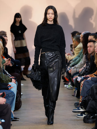 Model in Charcoal Viscose Wool Sweater, Black Nappa Leather Skirt, Black Cone Over The Knee Boots, Black Beacon Saddle Bag, and Black Leather Gloves